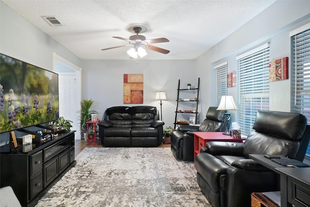 living room featuring a ceiling fan, a textured ceiling, visible vents, and wood finished floors