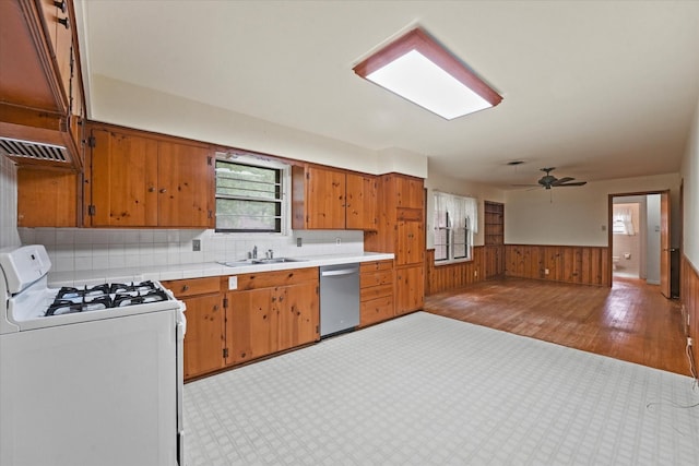 kitchen with white gas range oven, wainscoting, a sink, dishwasher, and light countertops