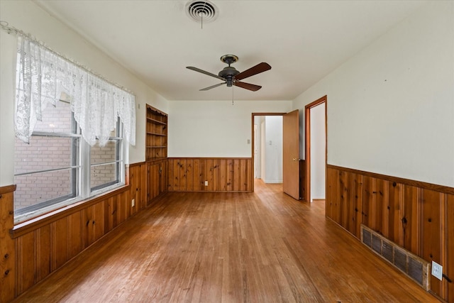 empty room with wooden walls, wainscoting, wood finished floors, and visible vents