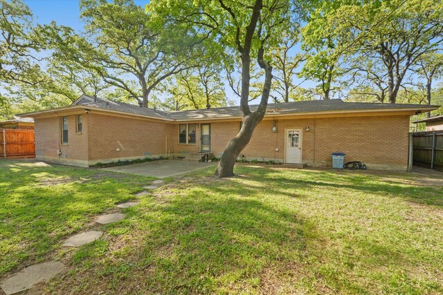 back of property featuring brick siding, a patio area, fence, and a lawn