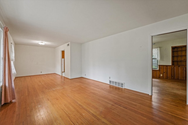 spare room featuring light wood-style floors, a wainscoted wall, and visible vents
