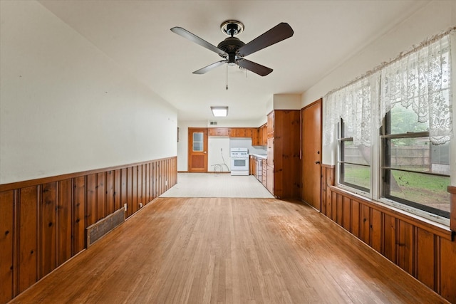 unfurnished living room featuring wooden walls, wainscoting, a ceiling fan, light wood-type flooring, and visible vents