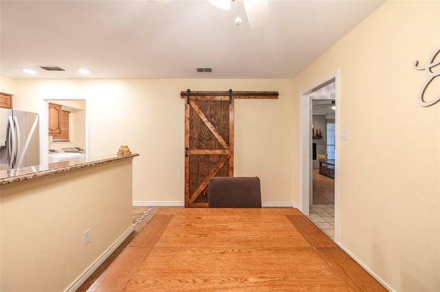 hallway featuring a barn door, light wood-type flooring, visible vents, and baseboards