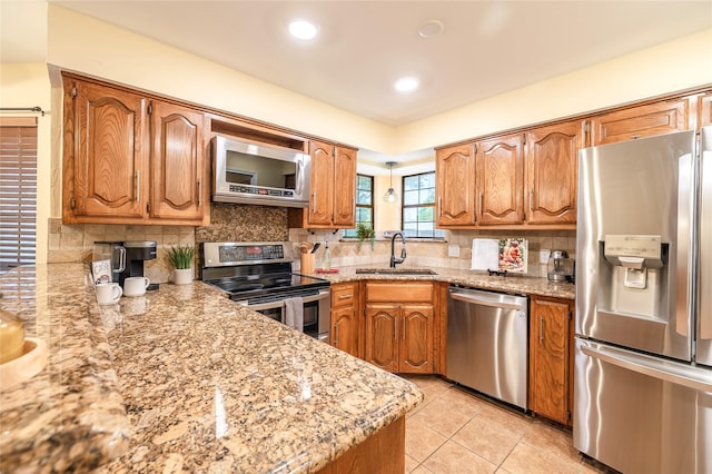 kitchen with brown cabinets, backsplash, light tile patterned floors, a sink, and appliances with stainless steel finishes