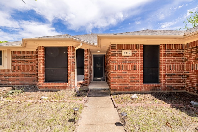 entrance to property featuring brick siding and roof with shingles