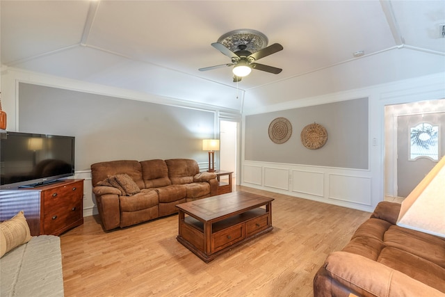 living area featuring light wood finished floors, wainscoting, vaulted ceiling, ceiling fan, and a decorative wall