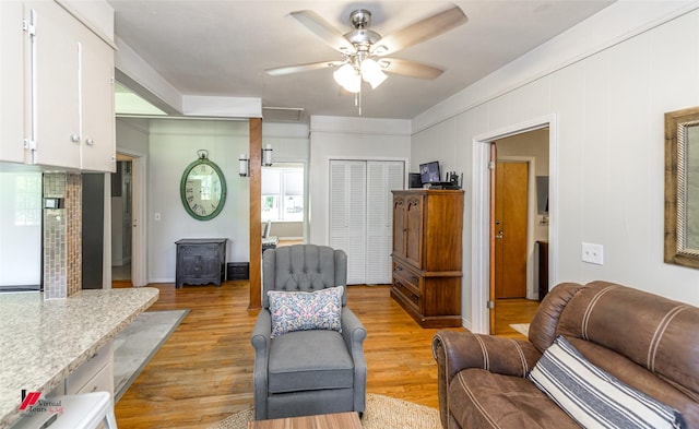 living area featuring light wood-style flooring, a wood stove, ceiling fan, and a healthy amount of sunlight