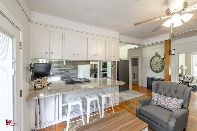 kitchen featuring tasteful backsplash, a breakfast bar area, ceiling fan, white cabinets, and a peninsula