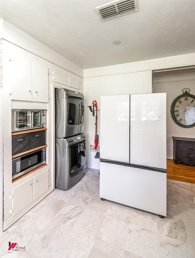 kitchen with stacked washer and clothes dryer, freestanding refrigerator, visible vents, and white cabinets