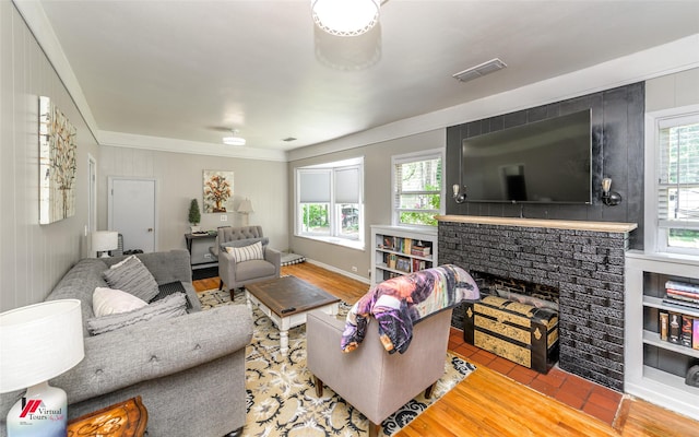 living area featuring a brick fireplace, wood finished floors, visible vents, and ornamental molding