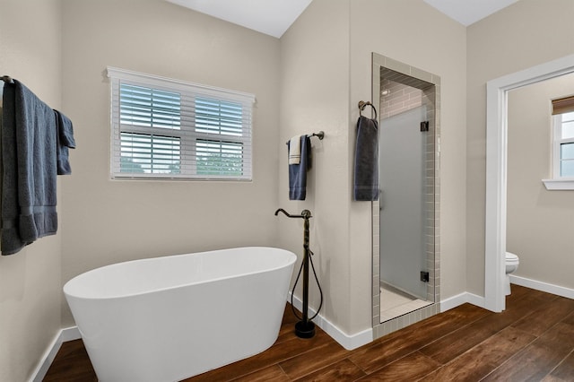 bathroom with wood finished floors, toilet, baseboards, a freestanding tub, and a stall shower