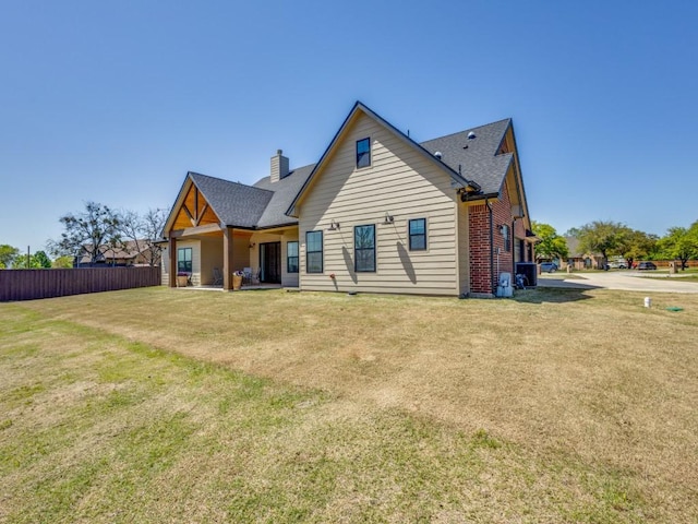 back of property with fence, a chimney, roof with shingles, and a yard