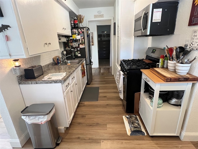108 E Neely Ave, Comanche, TX 76442 - kitchen with light wood finished floors, a sink, decorative backsplash, appliances with stainless steel finishes, and white cabinetry