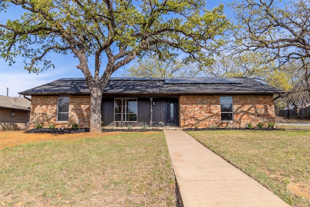 single story home featuring roof mounted solar panels, brick siding, and a front lawn