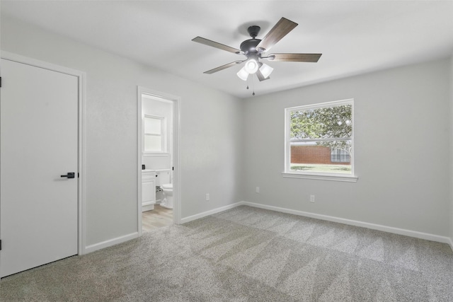 unfurnished bedroom with ensuite bathroom, baseboards, light colored carpet, and a ceiling fan
