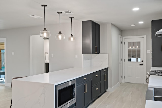 kitchen featuring a peninsula, stainless steel microwave, visible vents, baseboards, and light countertops