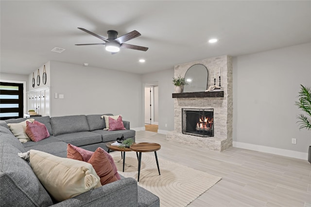 living area featuring light wood-type flooring, baseboards, a stone fireplace, and ceiling fan