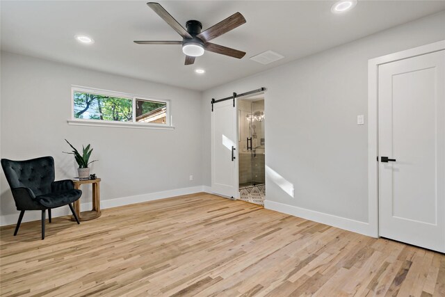 sitting room with a barn door, light wood-type flooring, visible vents, recessed lighting, and a ceiling fan