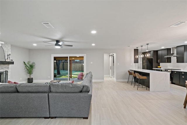 living area featuring a stone fireplace, visible vents, ceiling fan, and light wood-style flooring