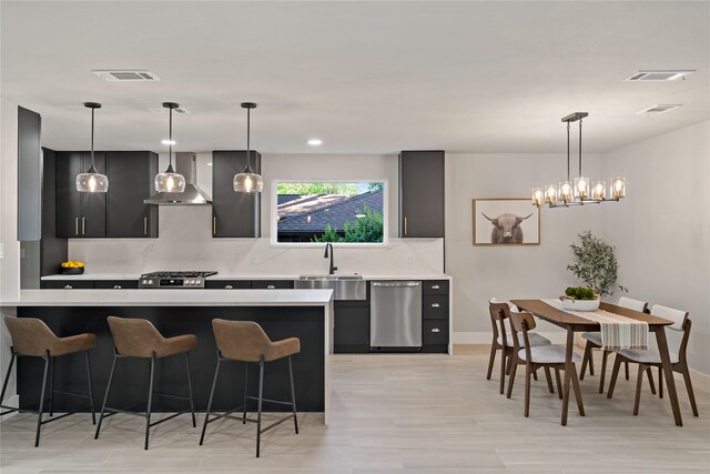 kitchen featuring a kitchen breakfast bar, a sink, dark cabinetry, wall chimney range hood, and dishwasher