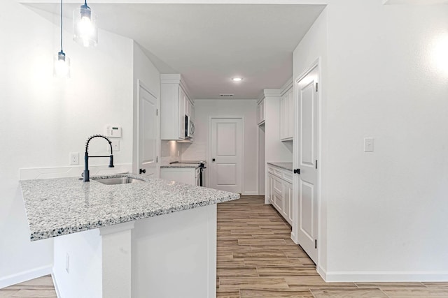 kitchen featuring white cabinets, a peninsula, light wood finished floors, a sink, and light stone countertops