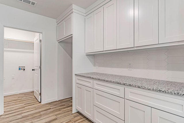 kitchen featuring decorative backsplash, light wood-style floors, white cabinetry, light stone countertops, and visible vents