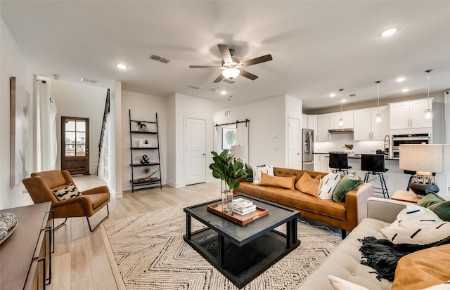 living room featuring a barn door, light wood-type flooring, ceiling fan, visible vents, and recessed lighting