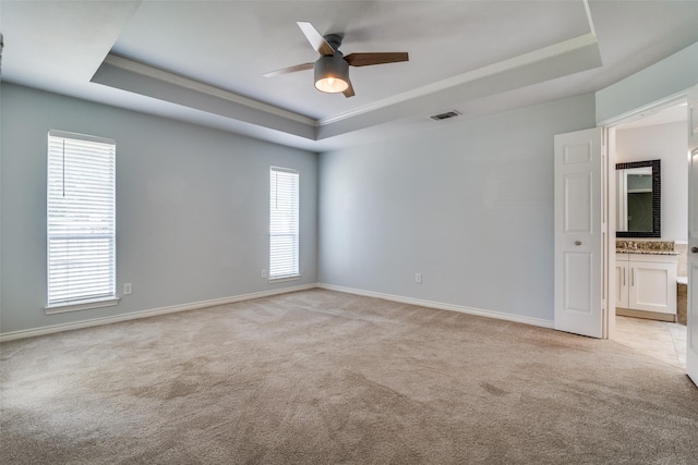empty room featuring baseboards, ceiling fan, light carpet, and a tray ceiling