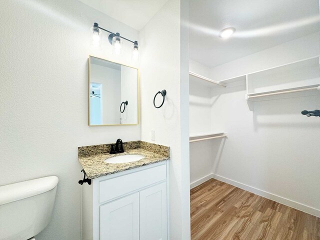 2408 Miller St, Denison, TX 75020 - bathroom with wood finished floors, a walk in closet, vanity, baseboards, and toilet