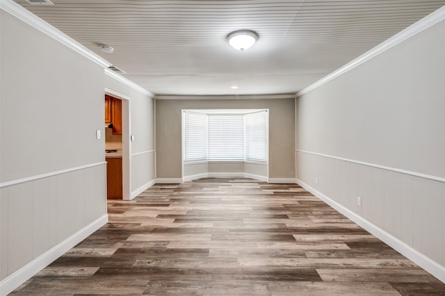 empty room featuring wainscoting, crown molding, and wood finished floors