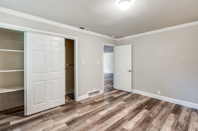 unfurnished bedroom with wood finished floors, visible vents, ornamental molding, a closet, and baseboards