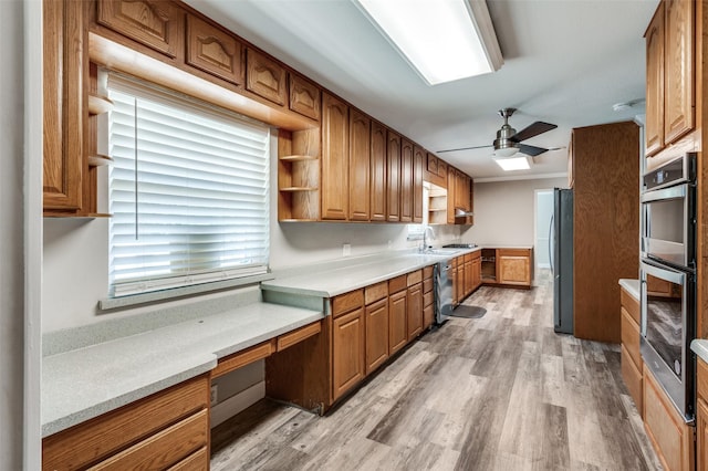 kitchen with a sink, built in desk, ceiling fan, brown cabinetry, and appliances with stainless steel finishes