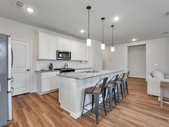 542 Freed Dr, Fate, TX 75087 - kitchen featuring appliances with stainless steel finishes, a sink, light wood-style floors, white cabinets, and a breakfast bar area