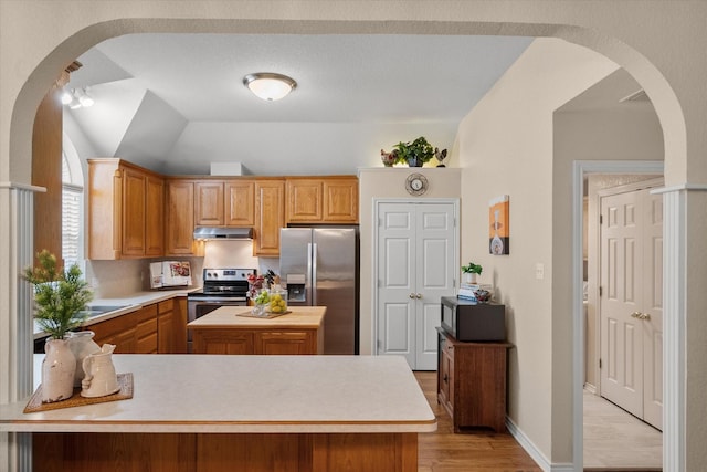 kitchen with under cabinet range hood, stainless steel appliances, light wood finished floors, and light countertops