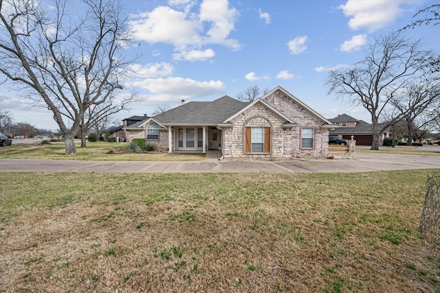 view of front of home featuring stone siding, a shingled roof, and a front lawn
