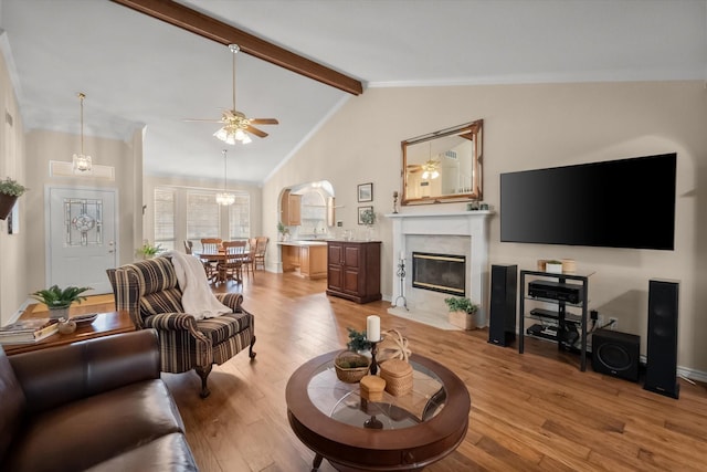 living area with ceiling fan, light wood-style floors, vaulted ceiling with beams, and a premium fireplace