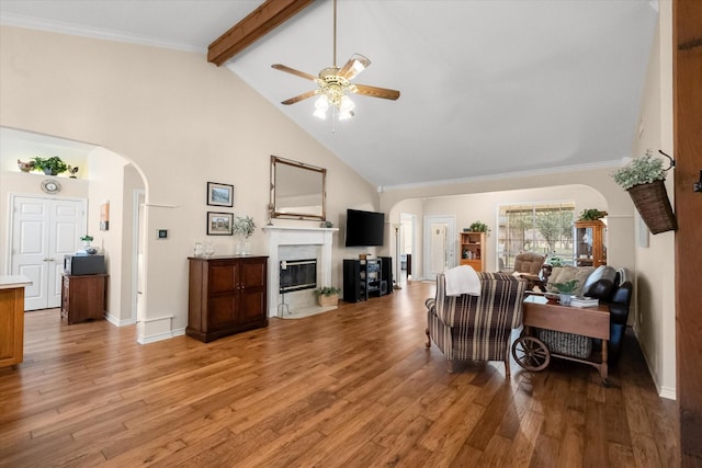 living area featuring a fireplace with flush hearth, arched walkways, beamed ceiling, a ceiling fan, and high vaulted ceiling