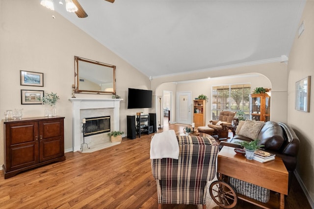 living area featuring a high end fireplace, light wood-style floors, ceiling fan, arched walkways, and ornamental molding