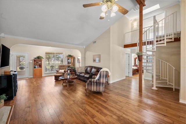 living room with light wood finished floors, arched walkways, a ceiling fan, stairs, and ornamental molding