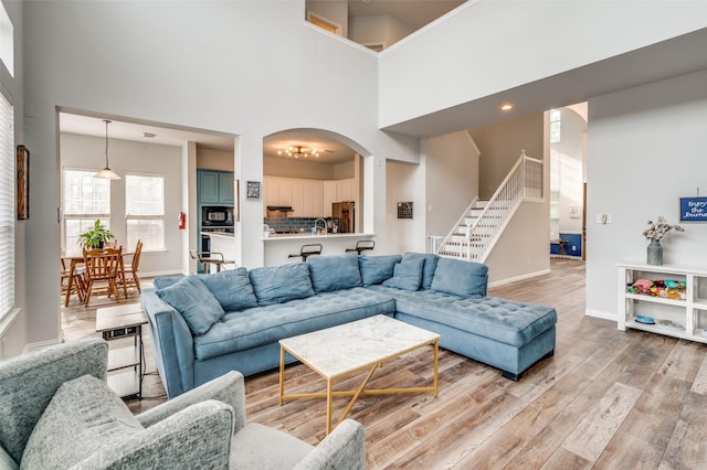 living area with stairway, a high ceiling, arched walkways, baseboards, and light wood-style flooring