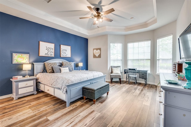 bedroom featuring ornamental molding, a tray ceiling, and light wood-style flooring
