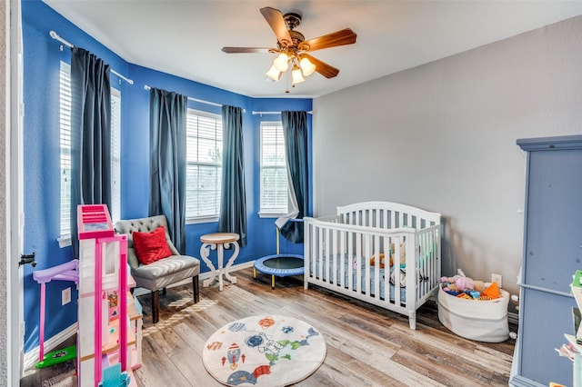 bedroom featuring a nursery area, wood finished floors, and a ceiling fan