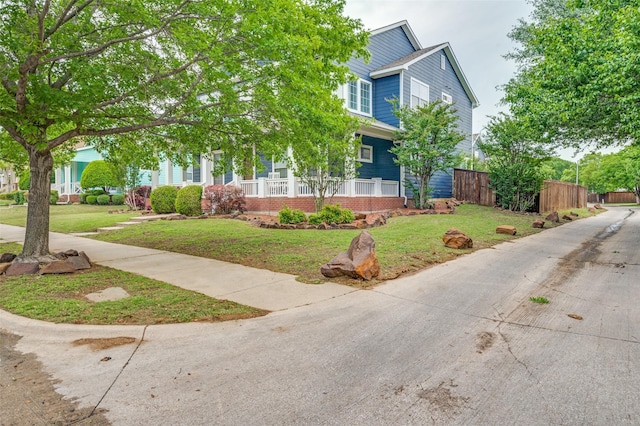 obstructed view of property featuring fence, covered porch, a front yard, and brick siding