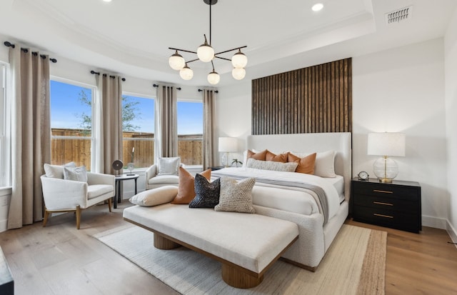 bedroom featuring light wood finished floors, a tray ceiling, recessed lighting, and a chandelier