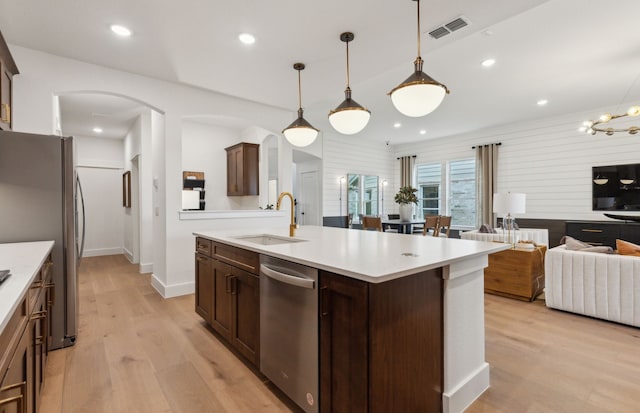 kitchen featuring stainless steel appliances, visible vents, a sink, arched walkways, and open floor plan