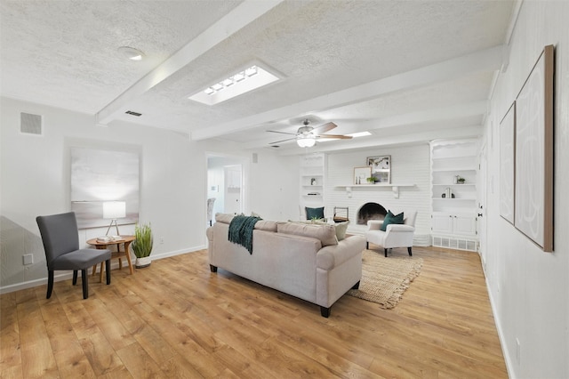 living area with light wood finished floors, beam ceiling, a textured ceiling, baseboards, and visible vents