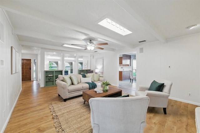 living room with ceiling fan, baseboards, beamed ceiling, and light wood-style flooring