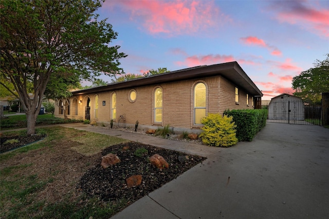 property exterior at dusk featuring driveway, a gate, and brick siding