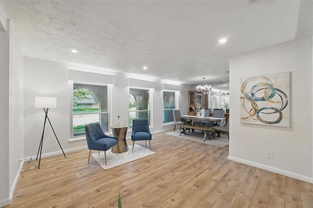 living area with wood finished floors, a textured wall, baseboards, a textured ceiling, and a notable chandelier