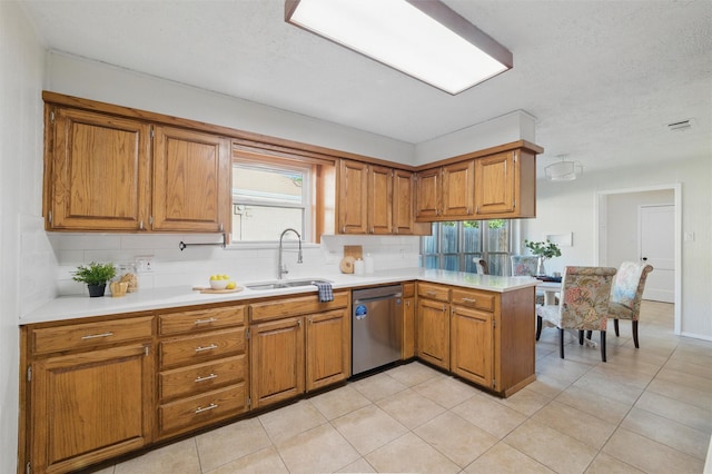 kitchen with a peninsula, stainless steel dishwasher, a sink, and brown cabinetry